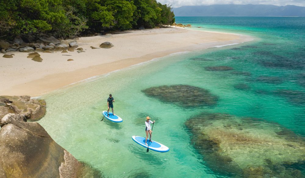 an aerial shot of two people stand-up paddling on the clear turquoise waters of Nudey Beach, Fitzroy Island